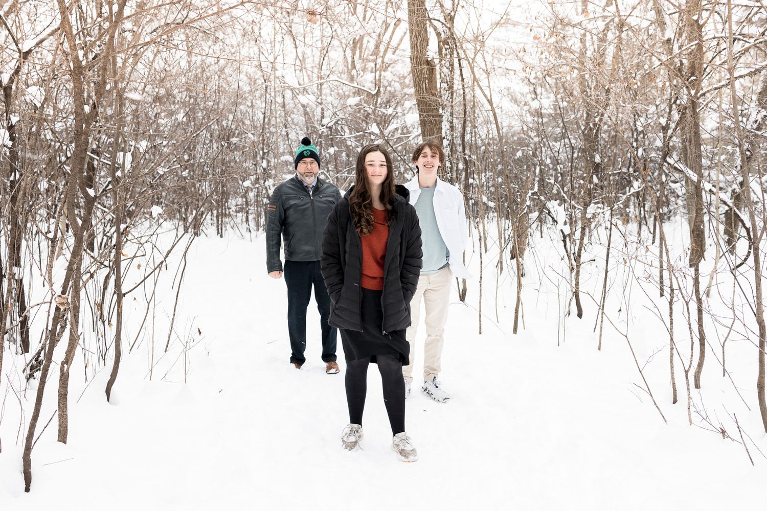 Three people walk through a snowy winter forest path.
