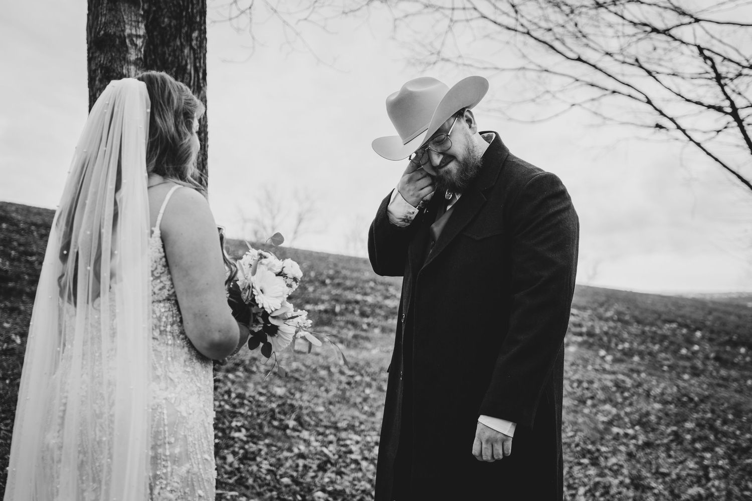 A black and white wedding photograph showing a bride in a veil with her bouquet and someone in dark winter attire outdoors.