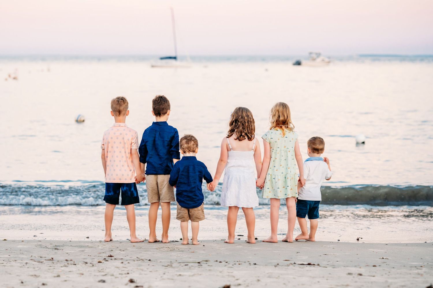 Five people stand at the edge of the shoreline at sunset with the ocean waves rolling in on a peaceful beach.