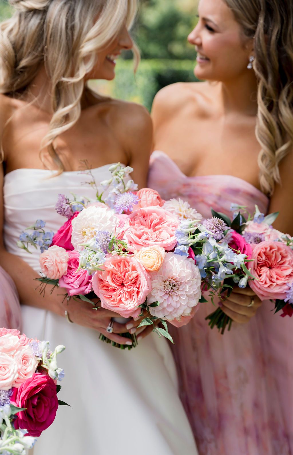 Bridesmaids holding lush pink and peach garden rose bouquets with greenery against pink and white dresses.