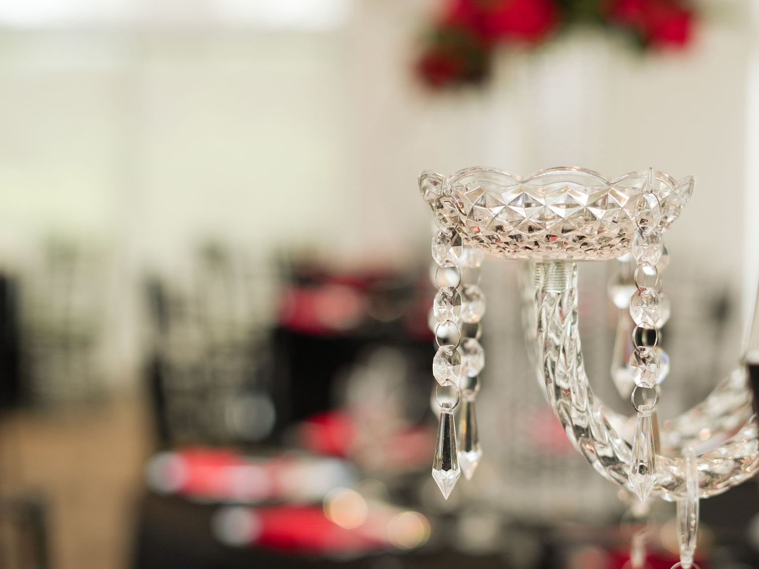 Crystal chandelier detail with hanging prisms against a blurred background with red accents.