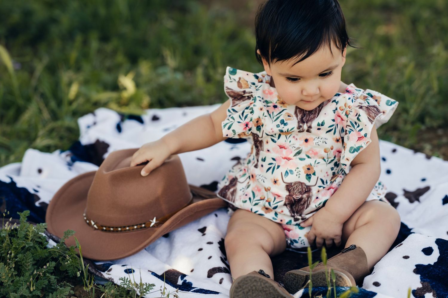Floral blanket spread on grass with scattered black and white cow print decorations.