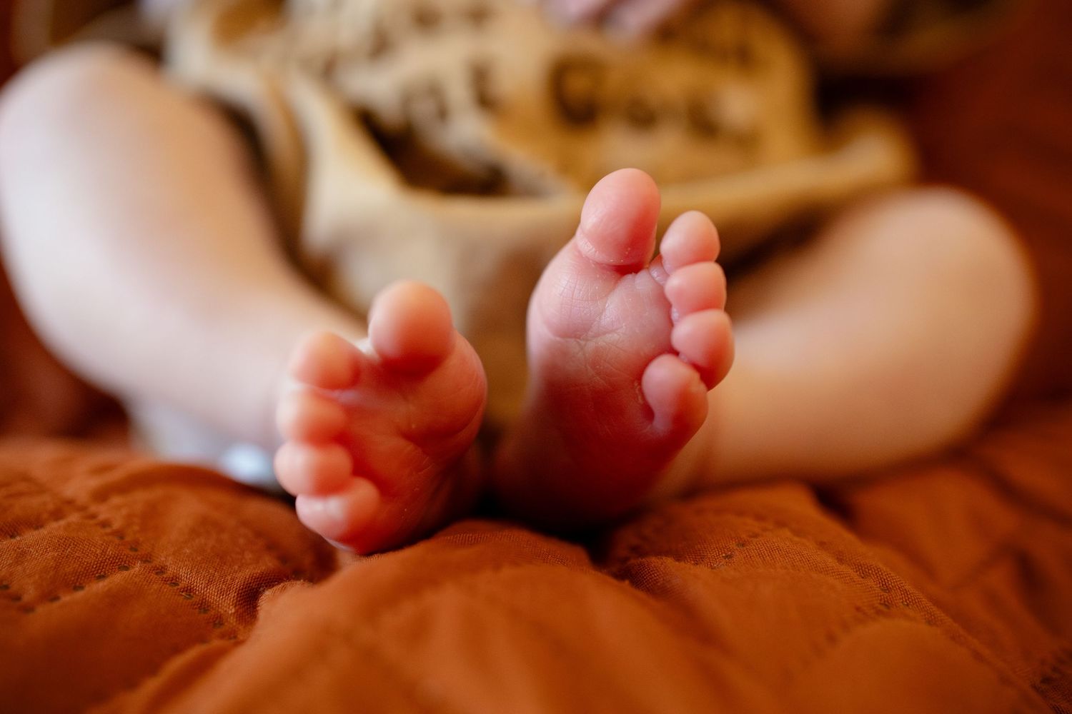 Close-up of a newborn baby's tiny bare feet and toes resting on a soft orange quilted blanket.