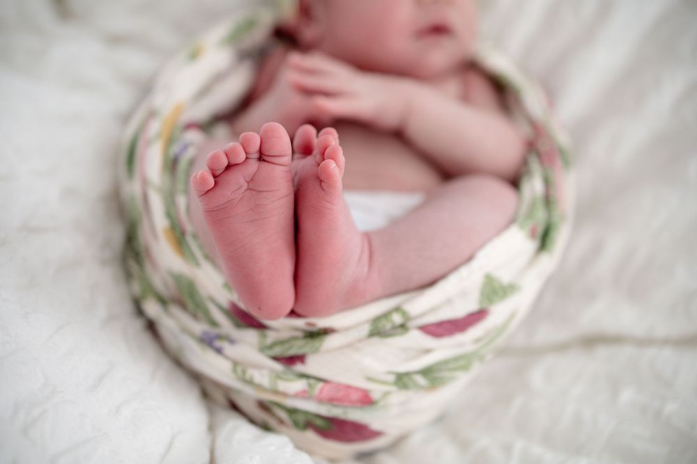 Newborn baby feet peeking out of a floral swaddle blanket, close-up photography of tiny infant toes.