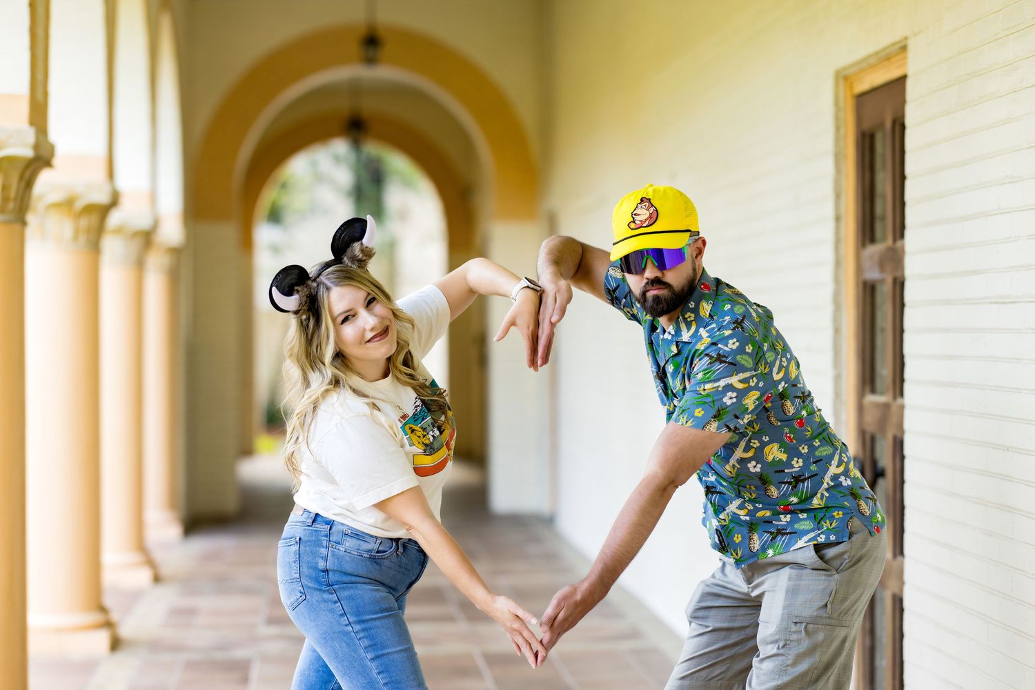 Couple posing playfully in a colorful hallway, woman wearing Mickey ears and man in tropical shirt and yellow cap.
