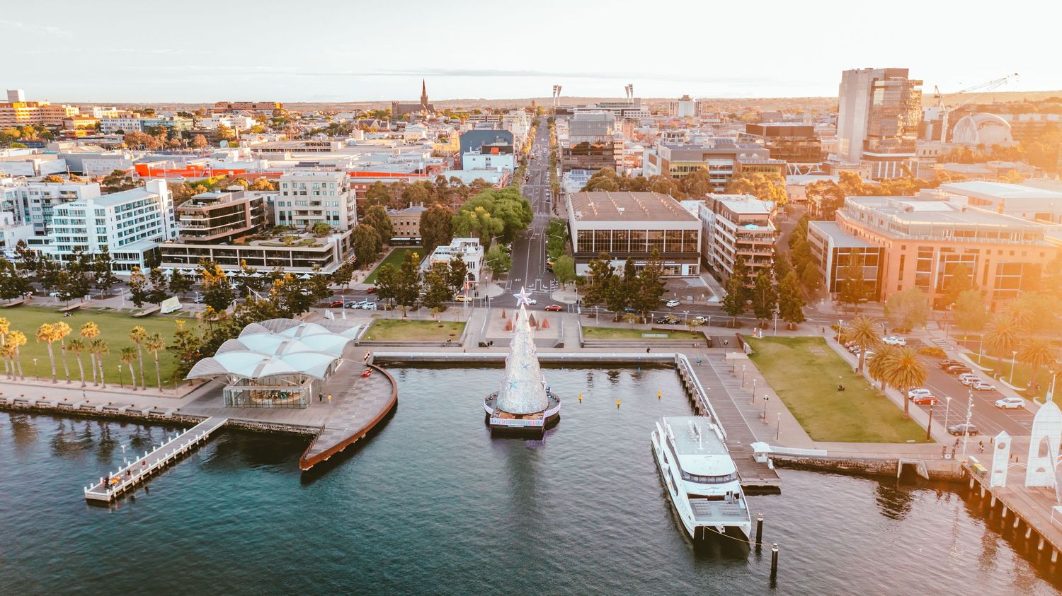 Aerial view of a waterfront city with boats and buildings during golden hour.