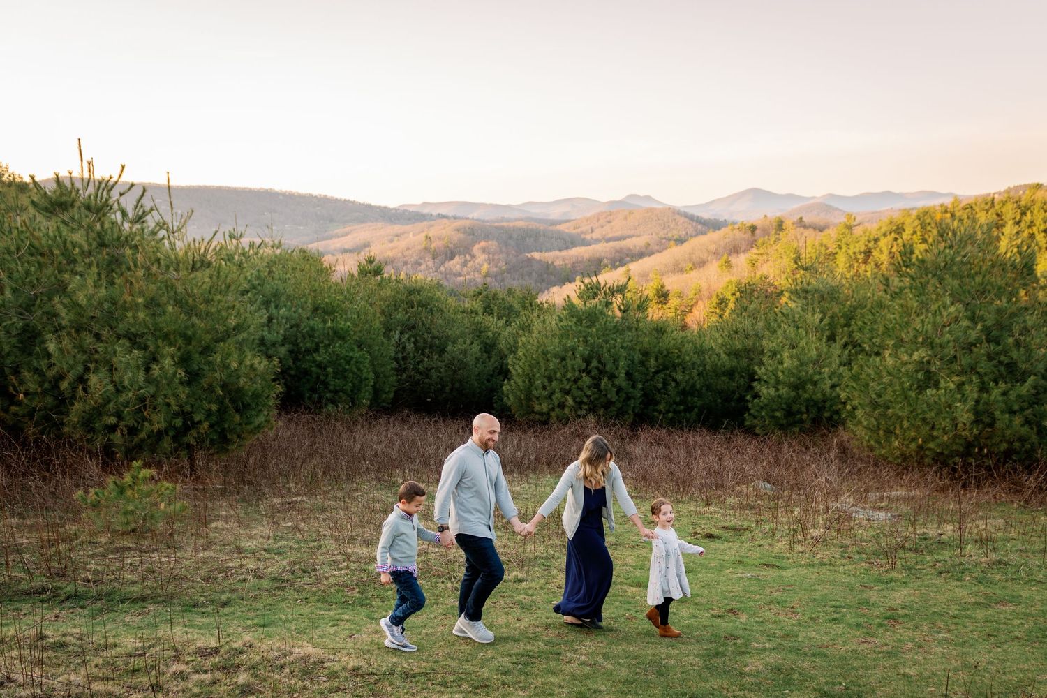 Family walking together on a grassy hilltop during golden hour with mountains in the background.