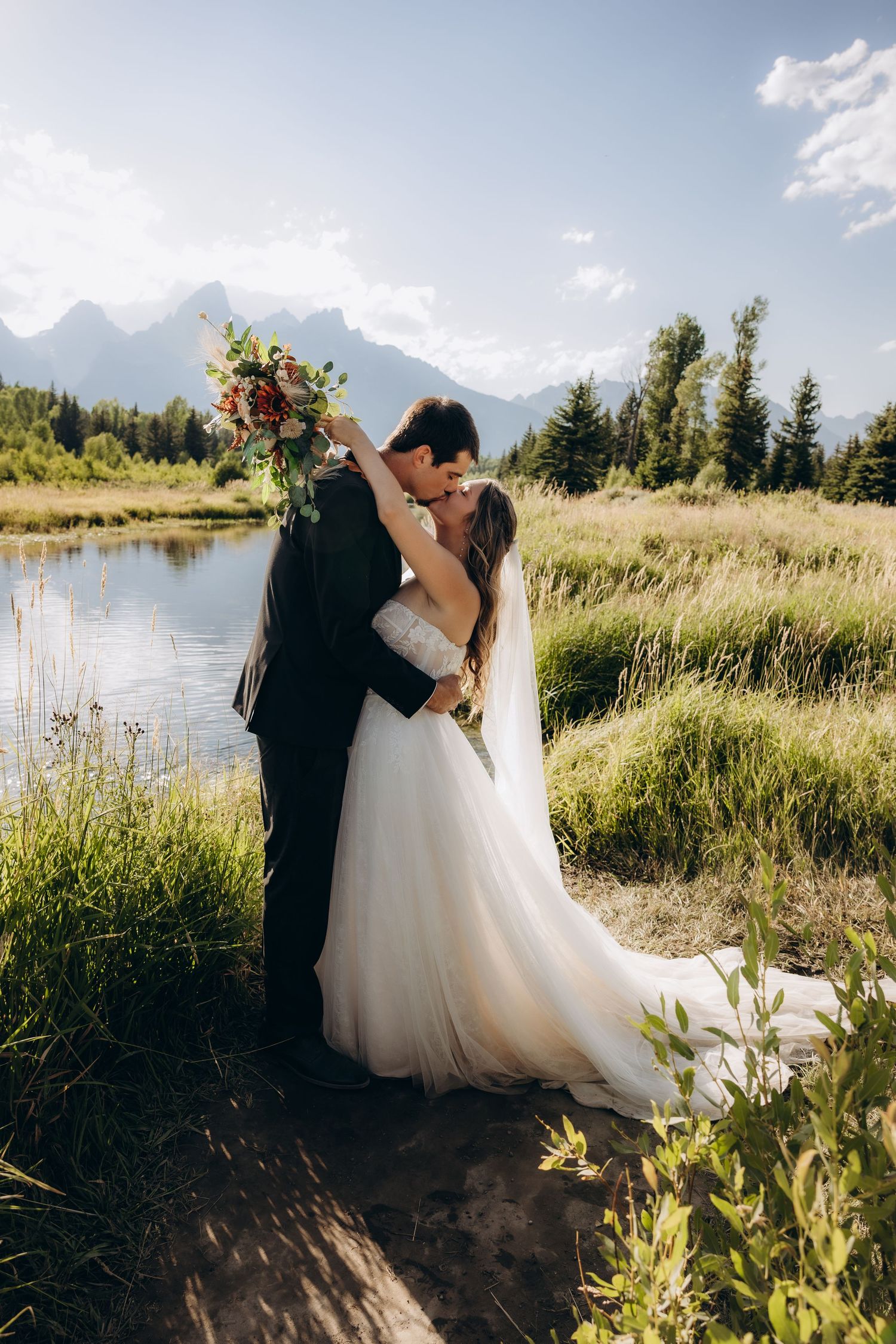 A wedding dress with flowing train billows in the wind against a backdrop of mountains and golden desert brush at sunset.