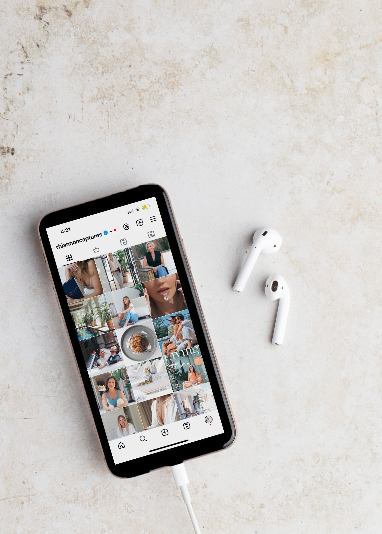Smartphone displaying social media grid layout with AirPods on white marble surface.