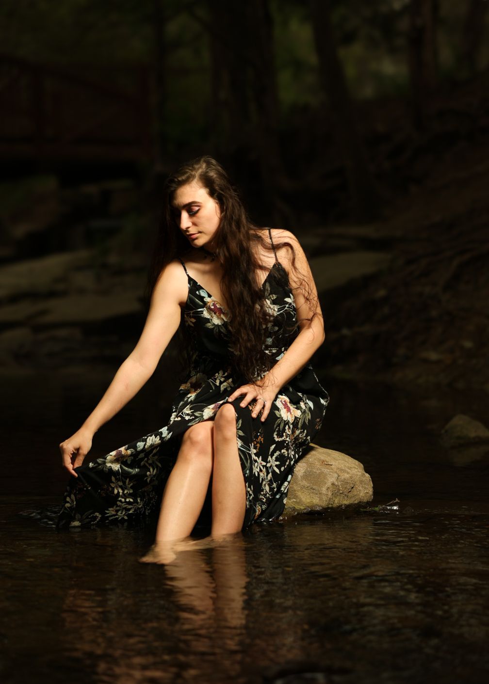 Person in dark patterned dress relaxing in shallow flowing water.