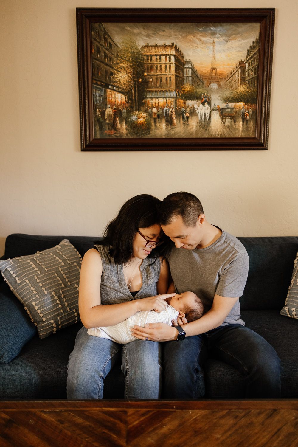 Parents cuddle their newborn baby on their sofa under a painting in their Bay Area home