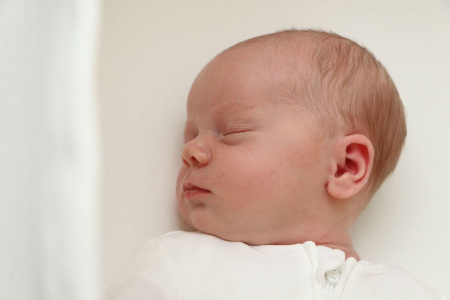 Peaceful sleeping newborn baby in white against white background.