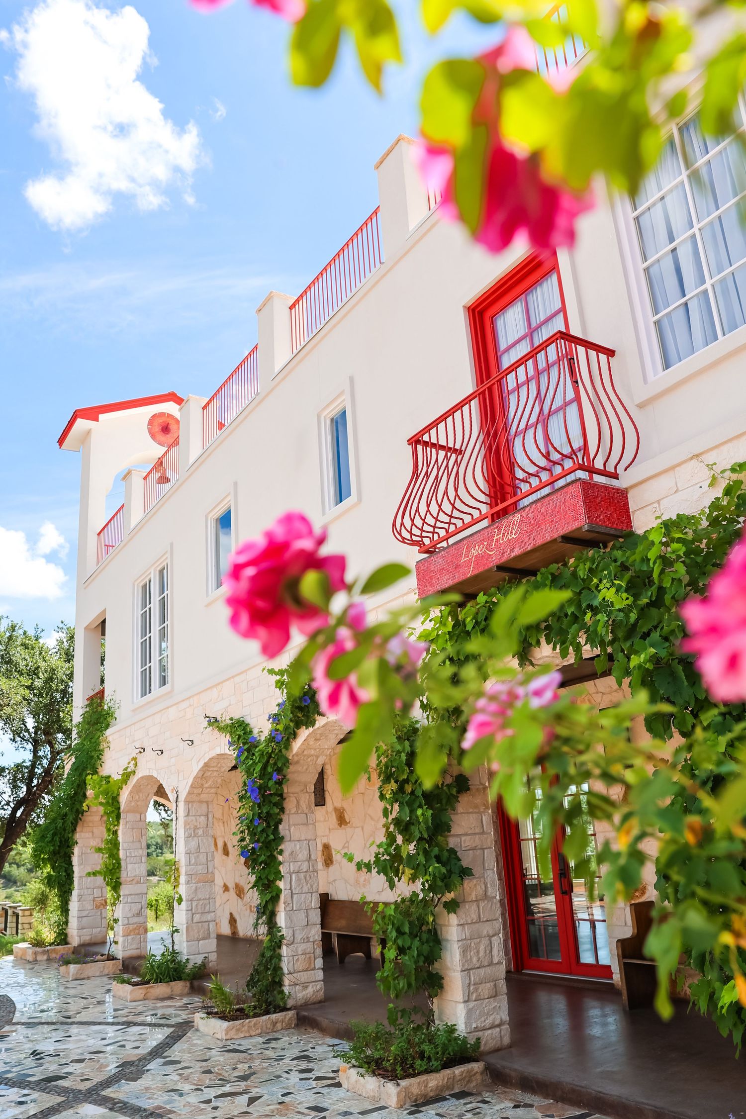 A Mediterranean-style building with red balconies and pink flowers framing the architectural details.