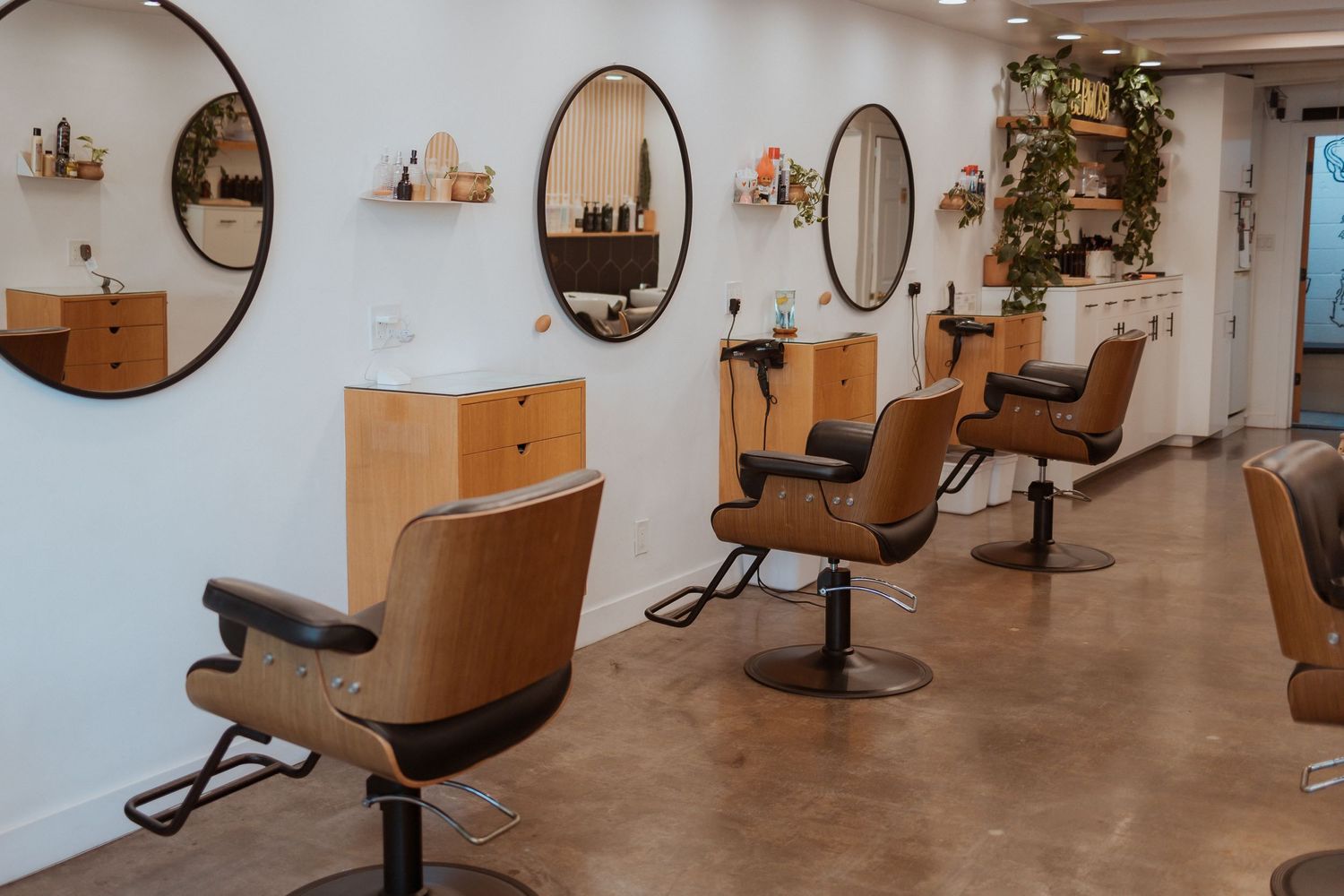 Modern hair salon interior with round mirrors and brown styling chairs.