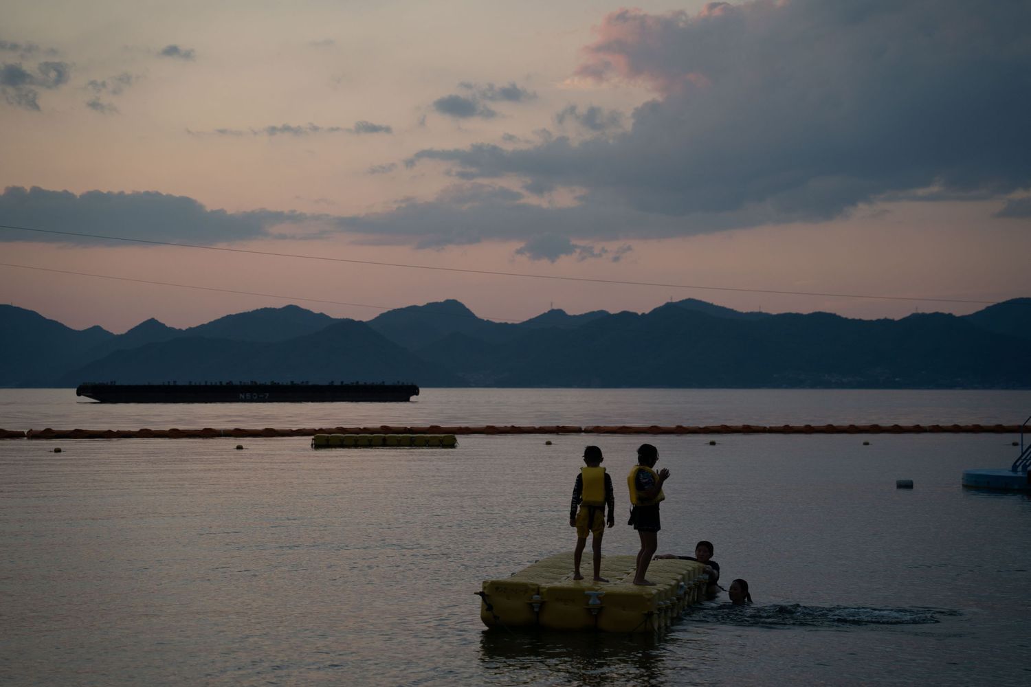 Silhouettes of people enjoying a sunset view over a tranquil bay with mountains in the background.