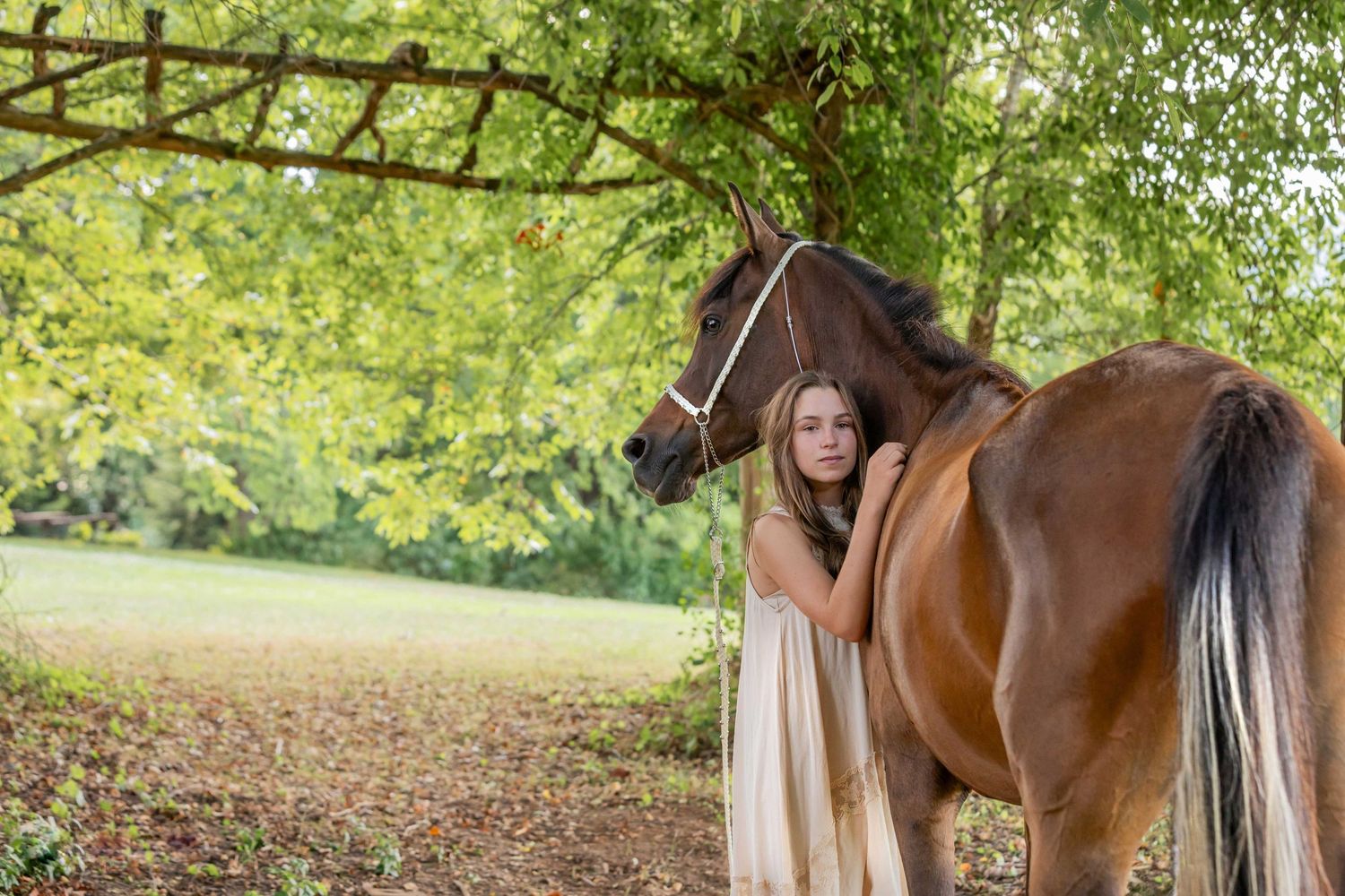 Horse and companion in flowing dress share tender moment under green canopy.