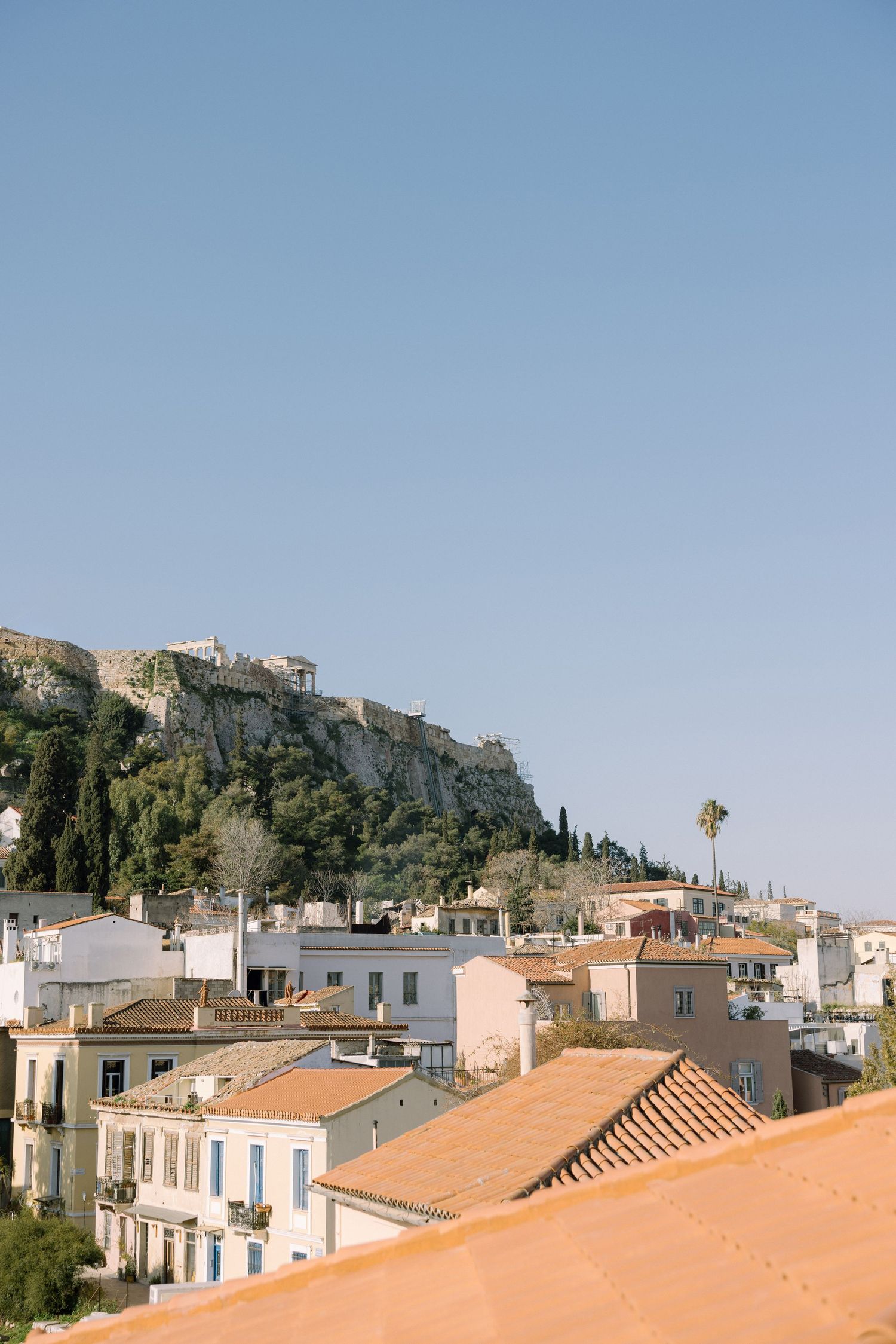 View of the Acropolis perched atop a rocky hill overlooking the Plaka neighborhood in Athens, Greece.