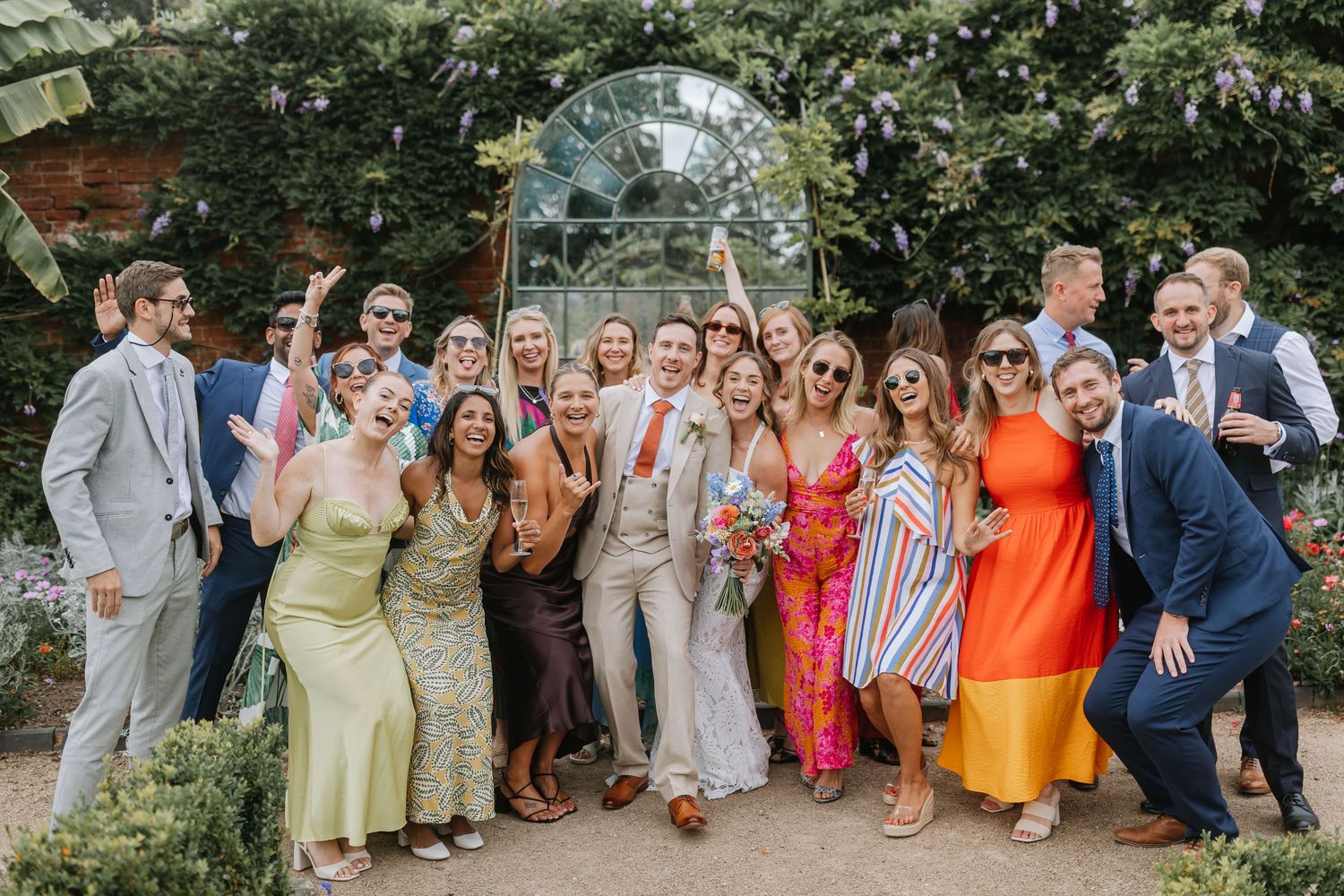 A group of wedding guests stand together for outdoor photos in colorful summer attire. Thorpe Garden Wedding. Wedding Photographer.