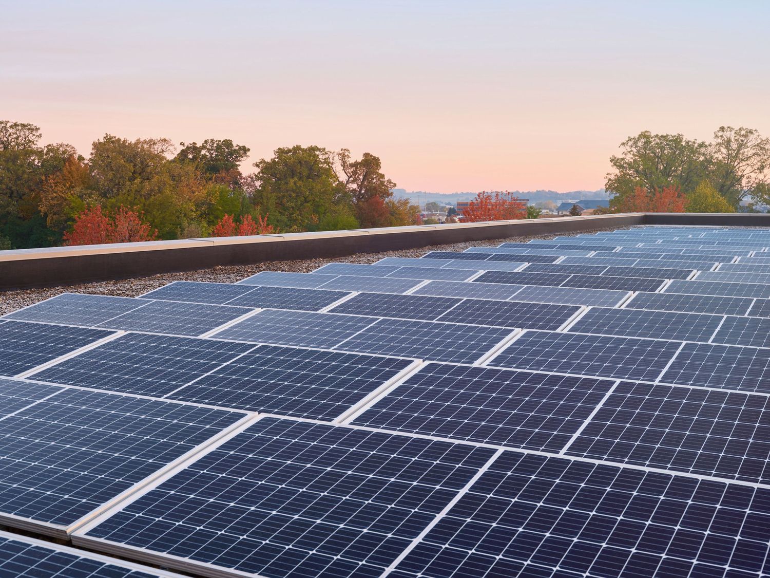 Solar panels installed on rooftop during sunset with blue sky and mountains in background.