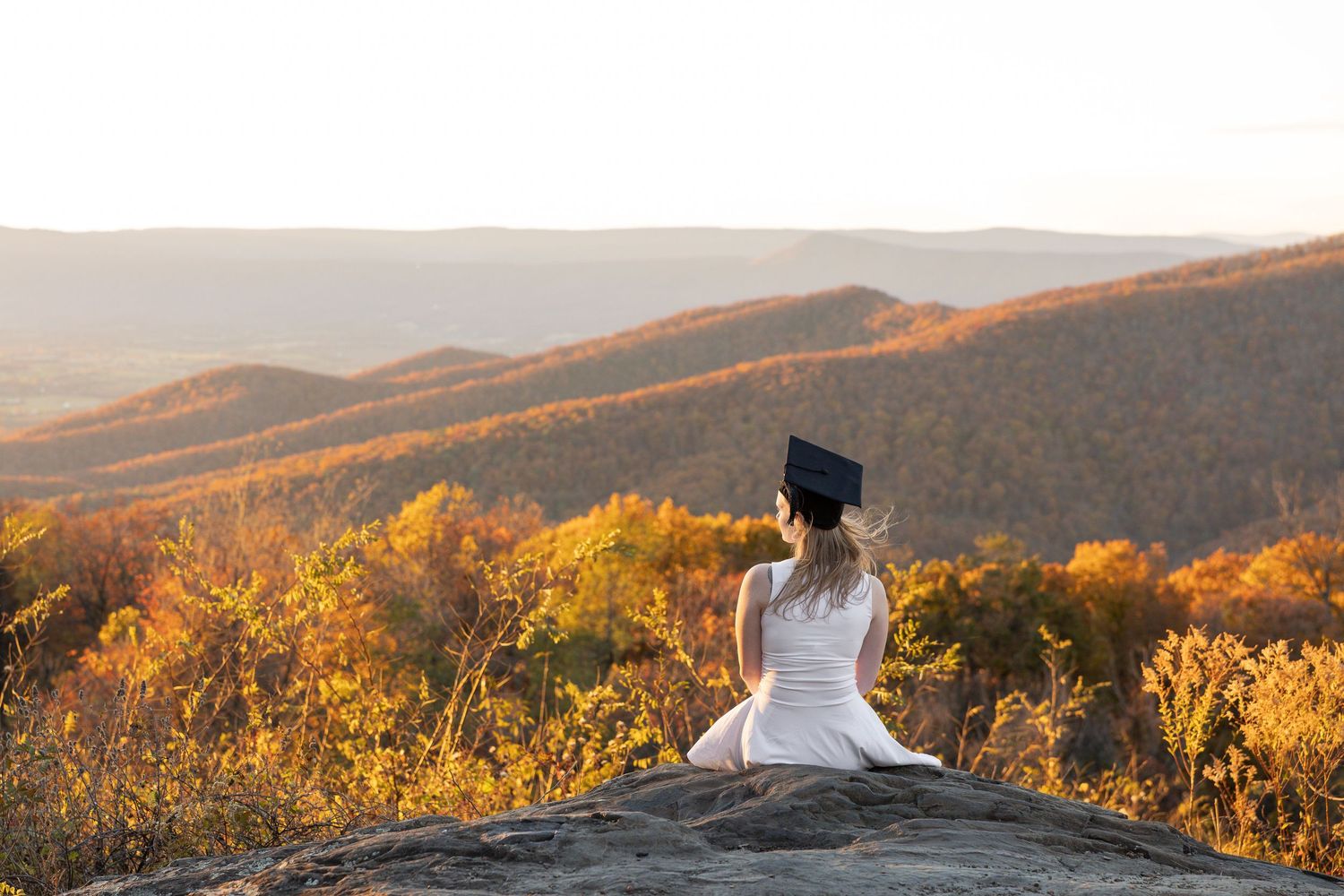 Couple embrace on mountain summit with expansive valley views below.