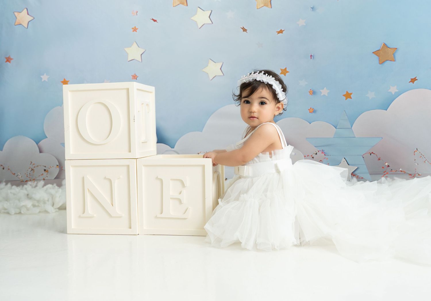 Dreamy baby portraits in a nursery setting with stars and clouds against a soft blue backdrop, surrounded by white blocks.