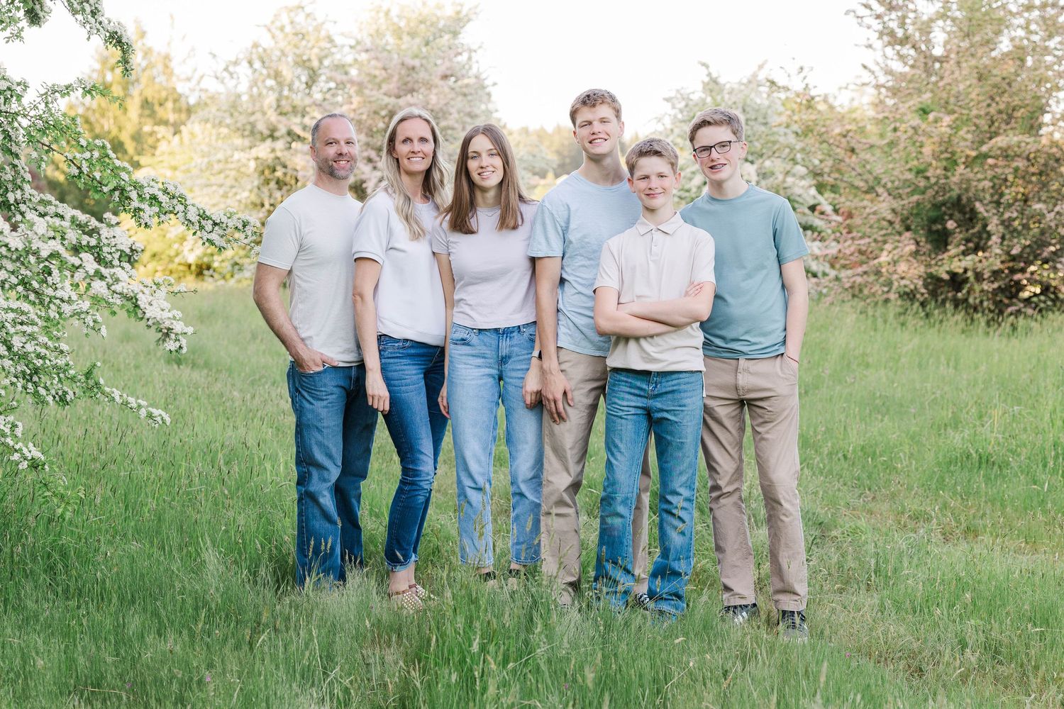 A family of six poses together smiling in a lush green meadow with blooming trees.
