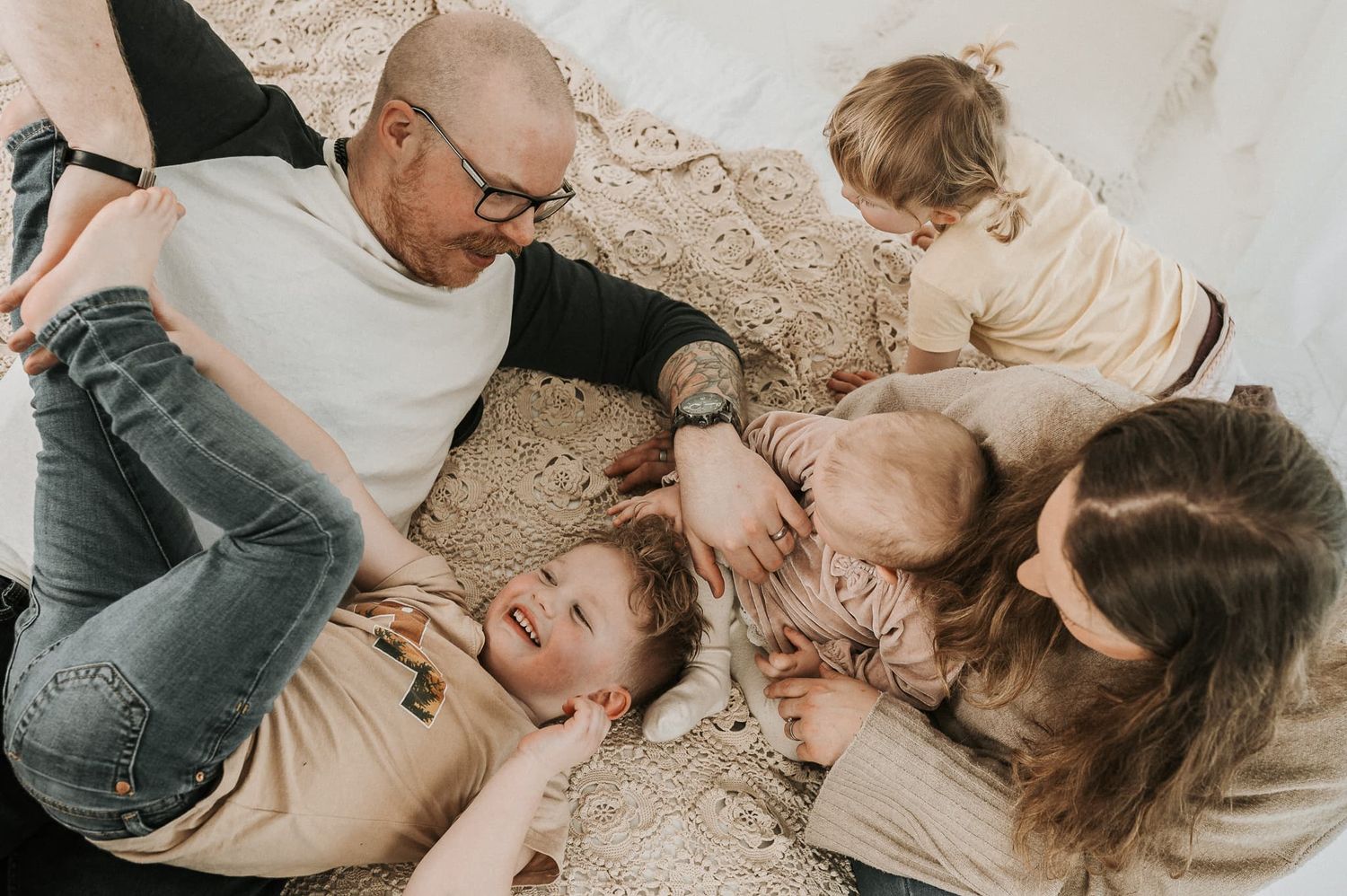 Mamma, pappa och tre barn ligger i en säng under en familjefotografering i studio hos Fotograf Veronica Eng, Jönköping Mullsjö.