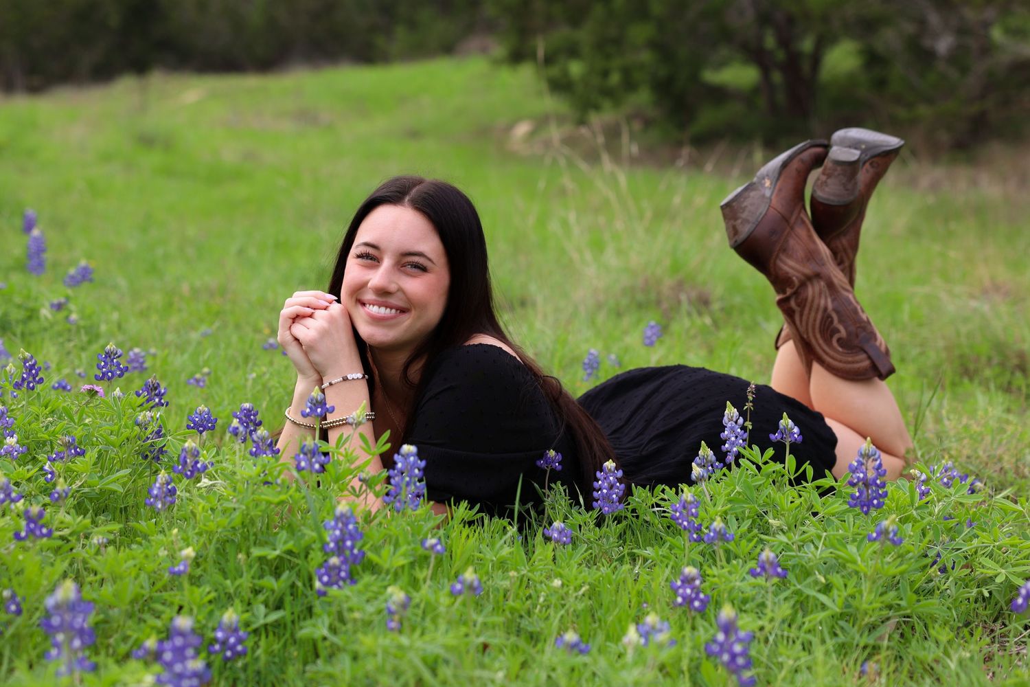 Person lying in a field of bluebonnets wearing boots and dark clothing in springtime.