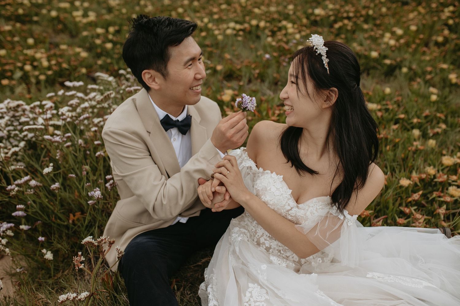 A couple in wedding attire shares romantic moments among Spring flowers at Windansea Beach in La Jolla.