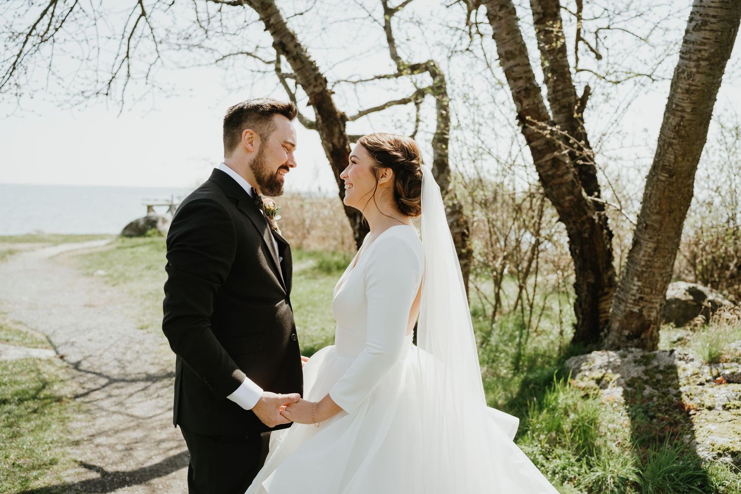 Romantic coastal wedding portrait with couple holding hands on a seaside path.