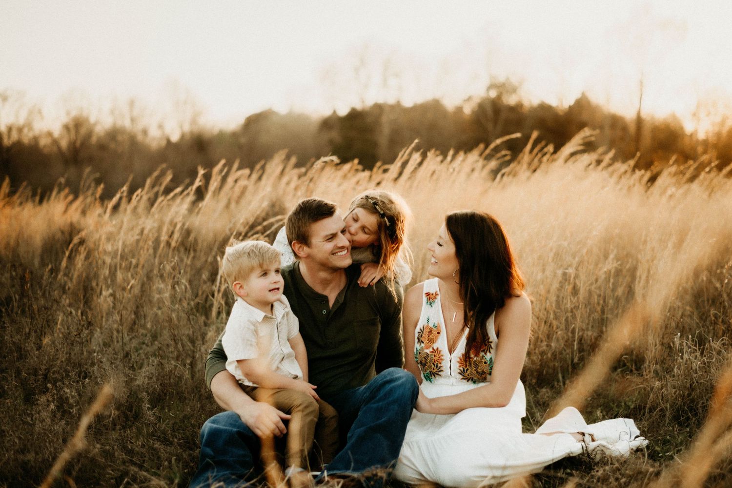 Family shares intimate moment in tall grass during golden hour.