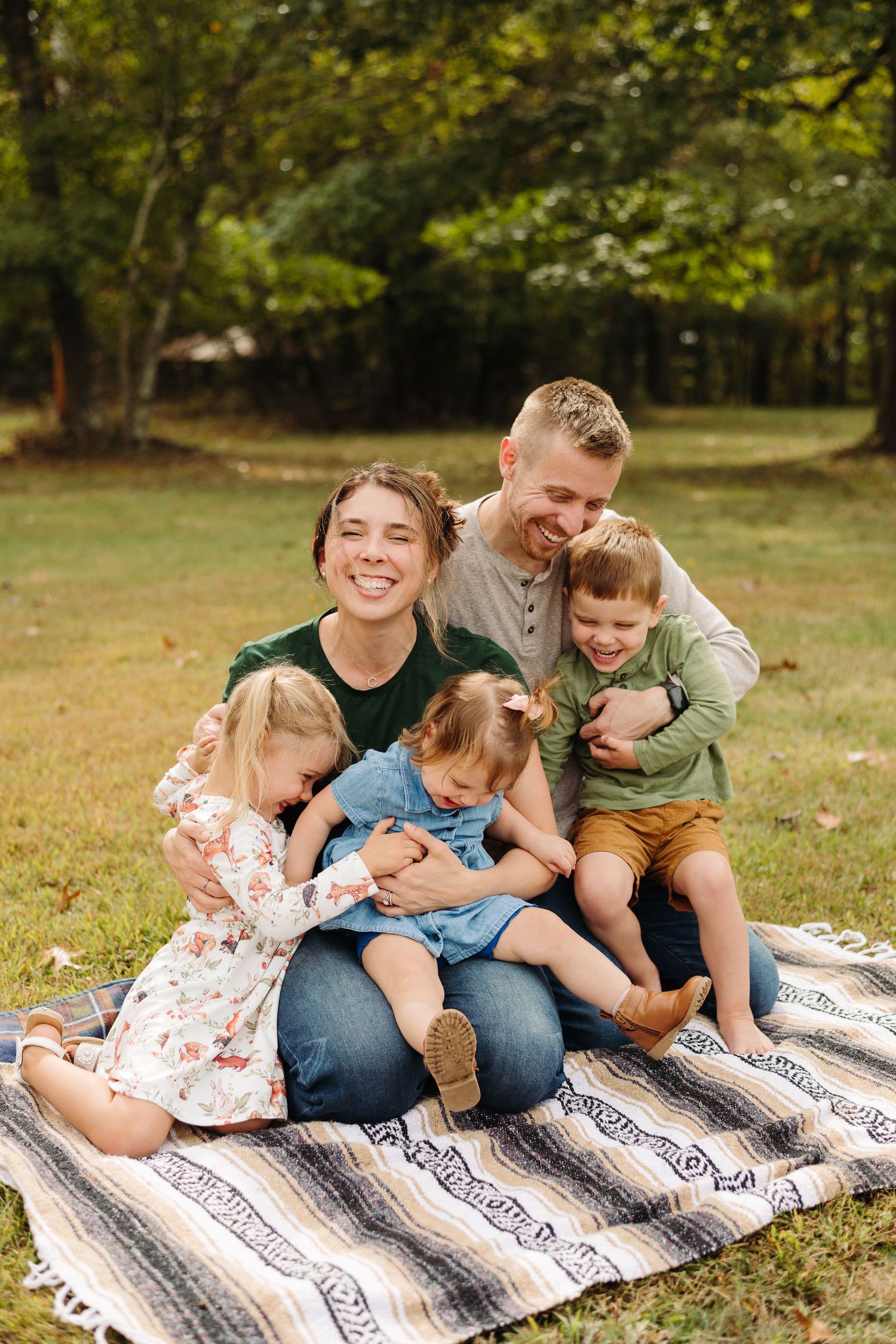 Family sitting together on striped blanket outdoors enjoying playful moments in nature.
