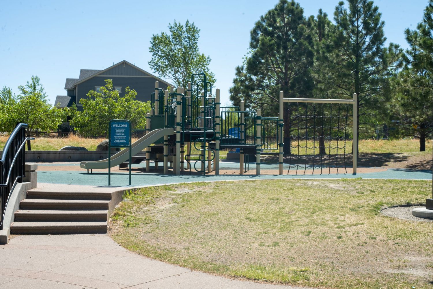 Outdoor playground with slides and climbing structures surrounded by trees and rubber safety surfacing.