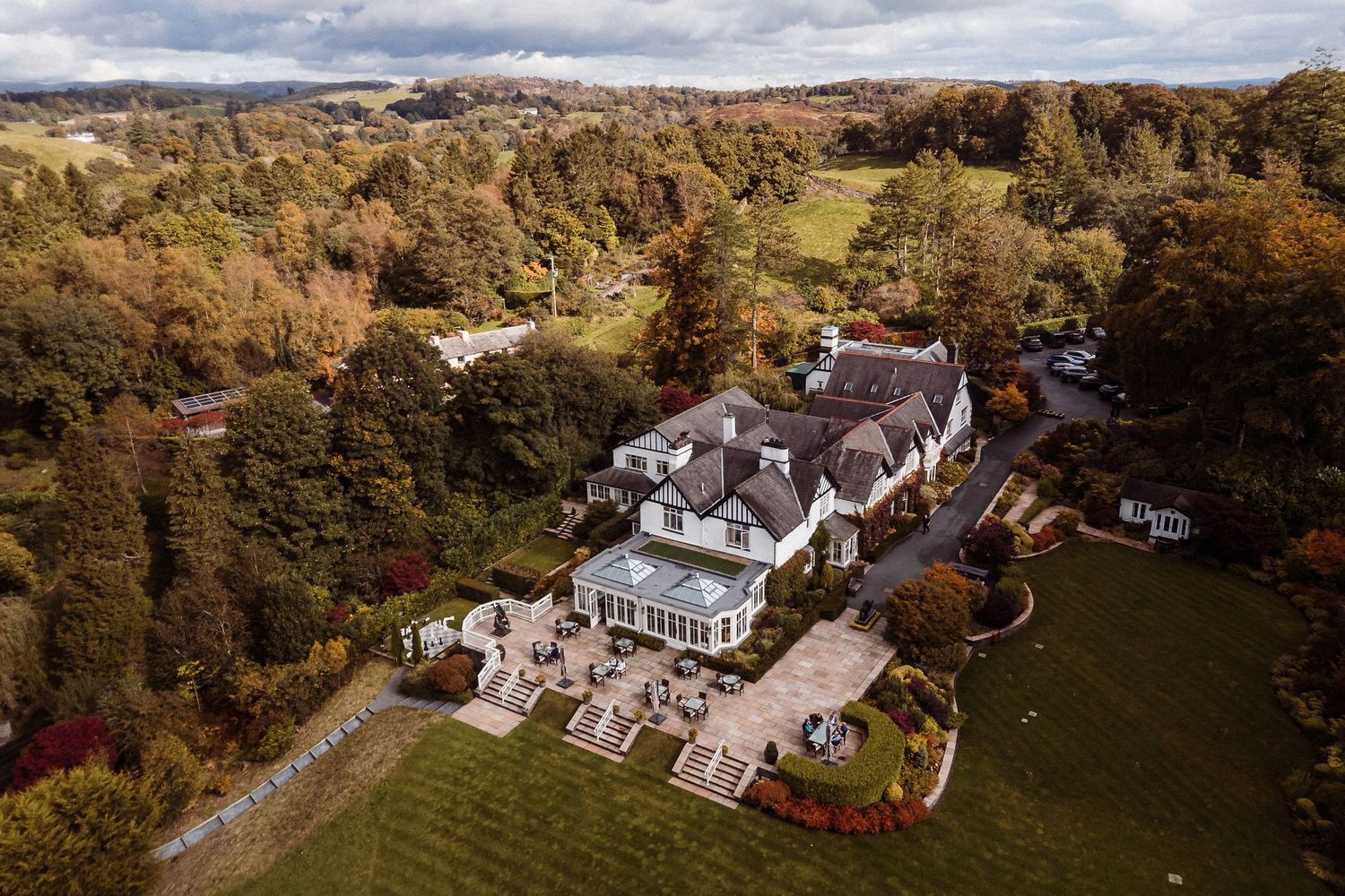 Aerial view of Linthwaite House surrounded by trees on a peninsula, with misty hills in the background.