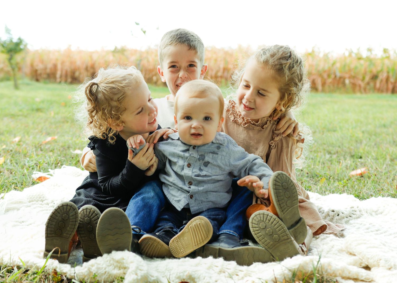 A group relaxes together on a cozy white blanket outdoors during a sunny autumn day.