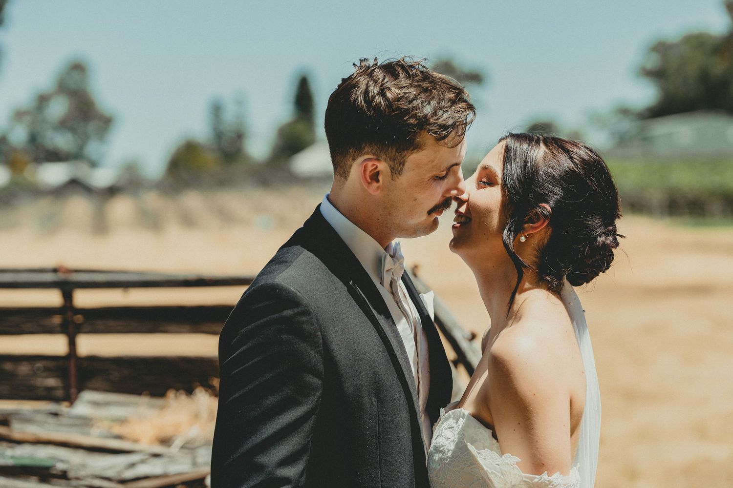 Wedding couple stands near modern glass buildings at sunset in an urban waterfront setting.