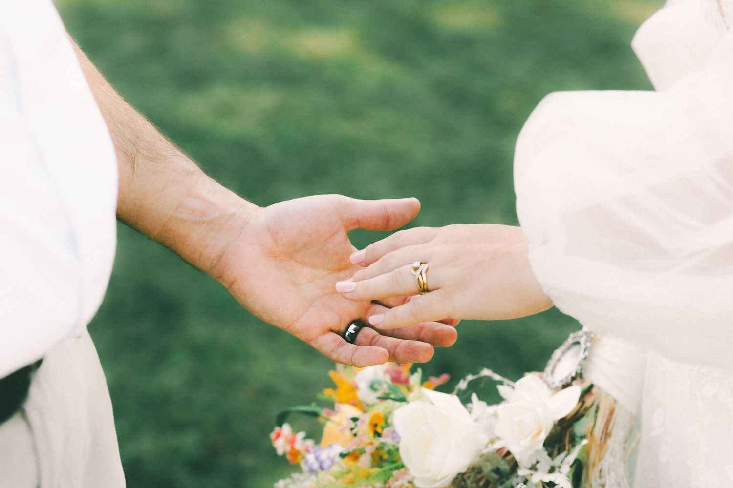 Close-up of hands holding delicate white and pink floral wedding bouquets against green background.