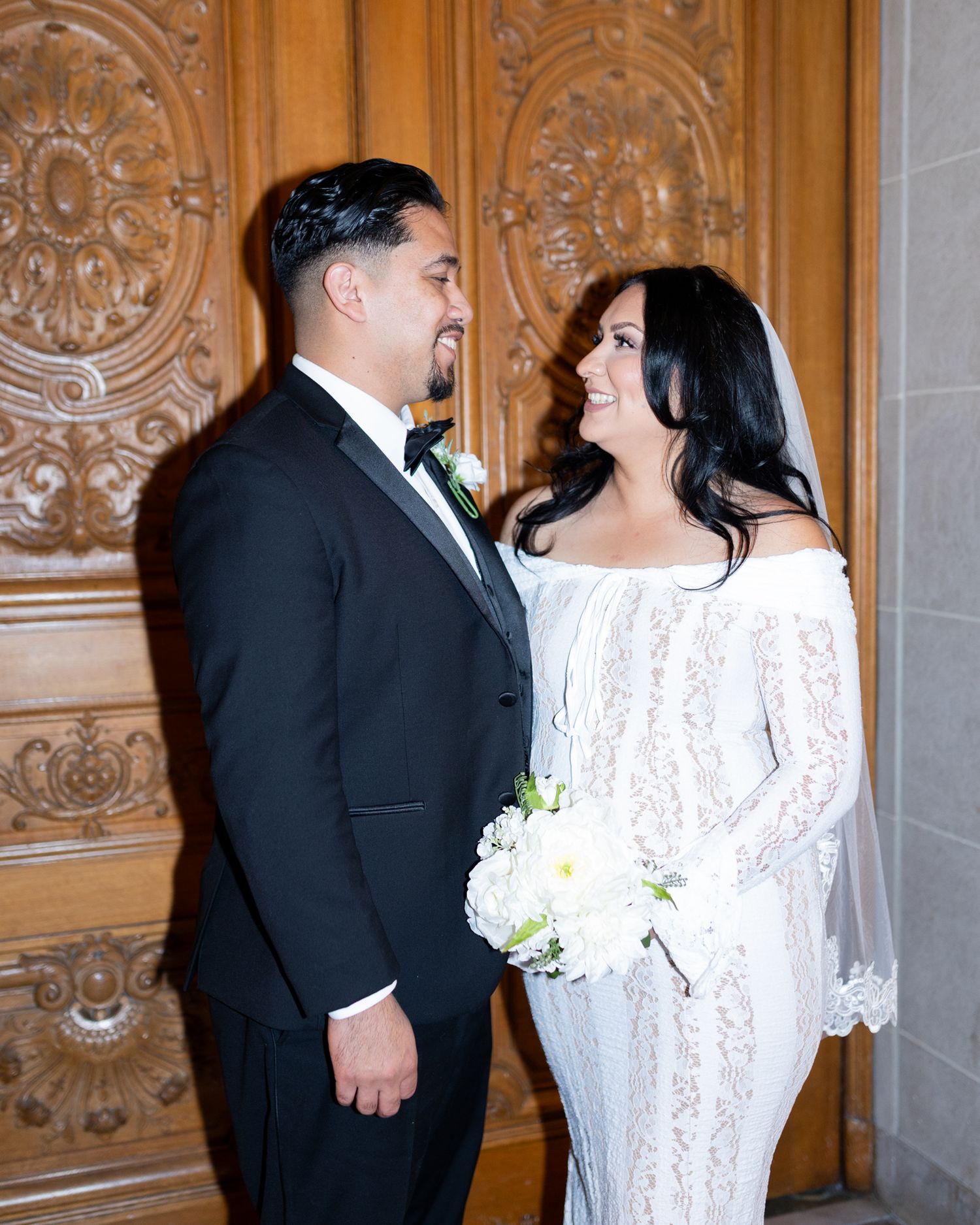 Elegant bride and groom holding hands at San Francisco City Hall wedding, wearing formal attire with white floral bouquet.