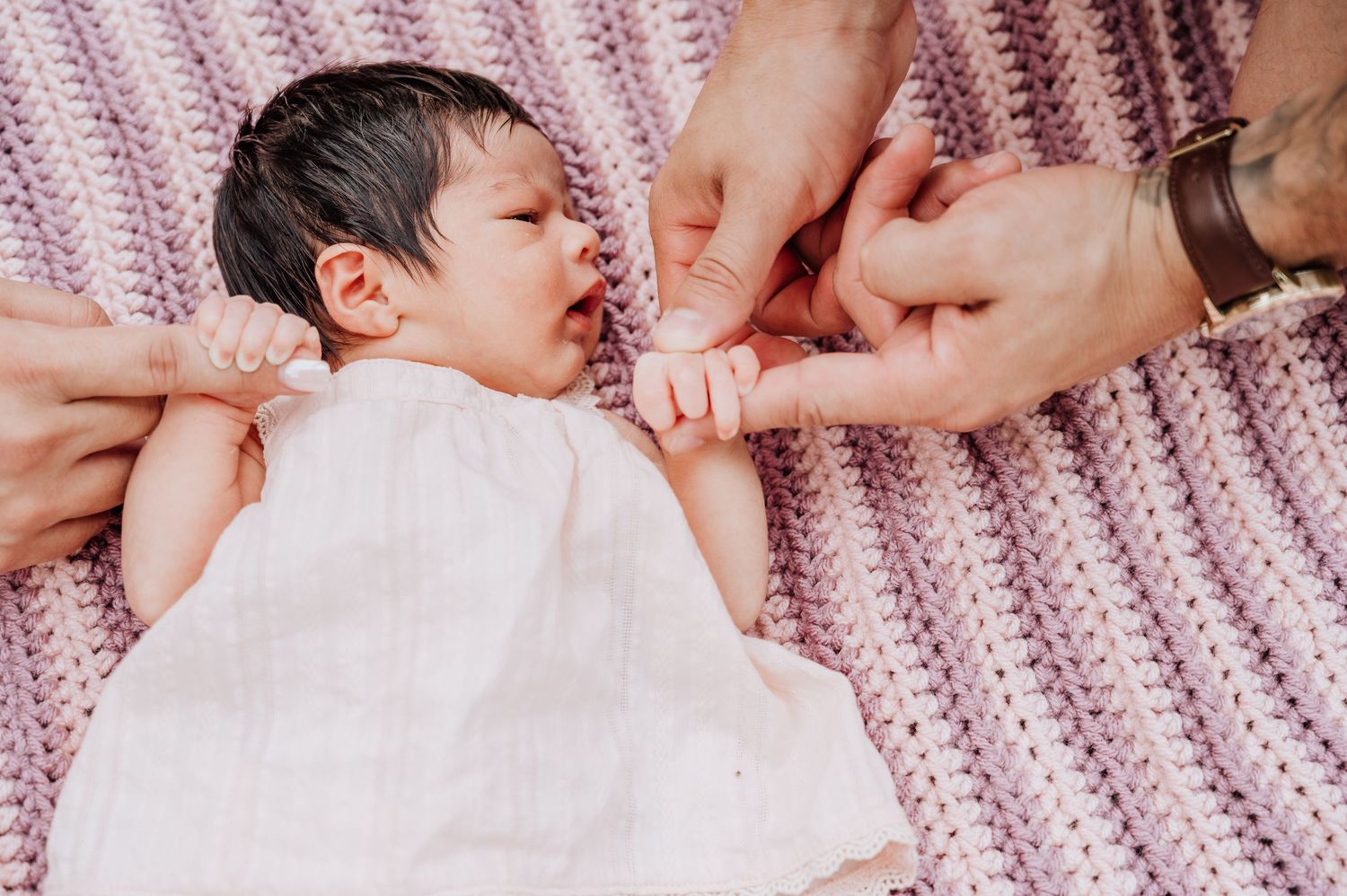 newborn baby girl holding the fingers of mom and dad