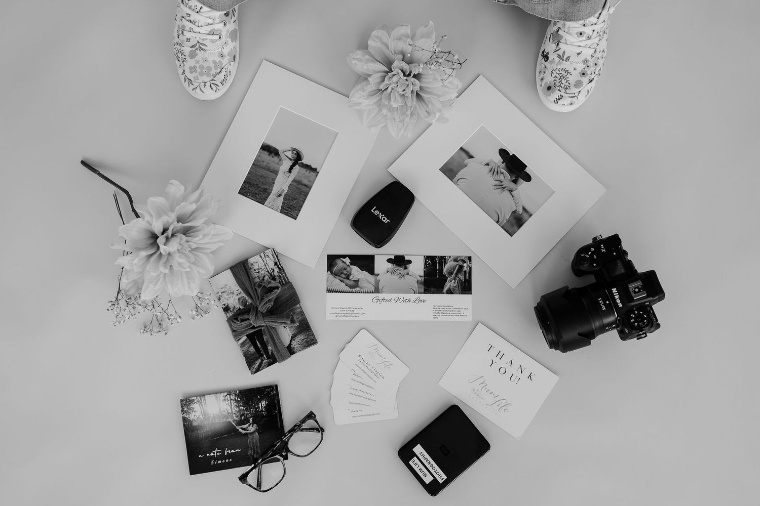 Black and white photo of cameras, photographs, and floral decorations arranged in a flat lay composition.