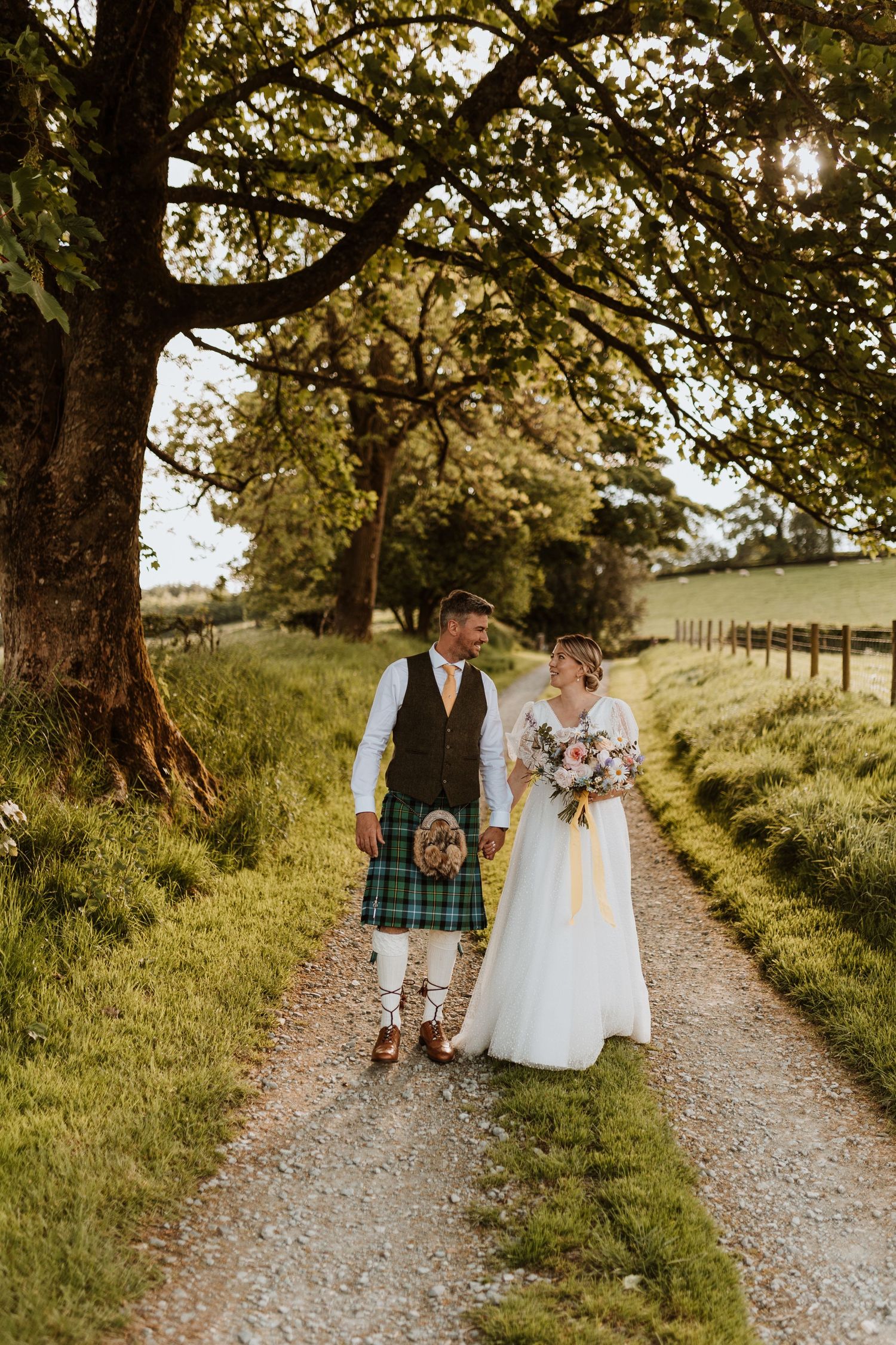 Romantic couples embrace in golden sunlit meadow surrounded by trees during an outdoor photo session.
