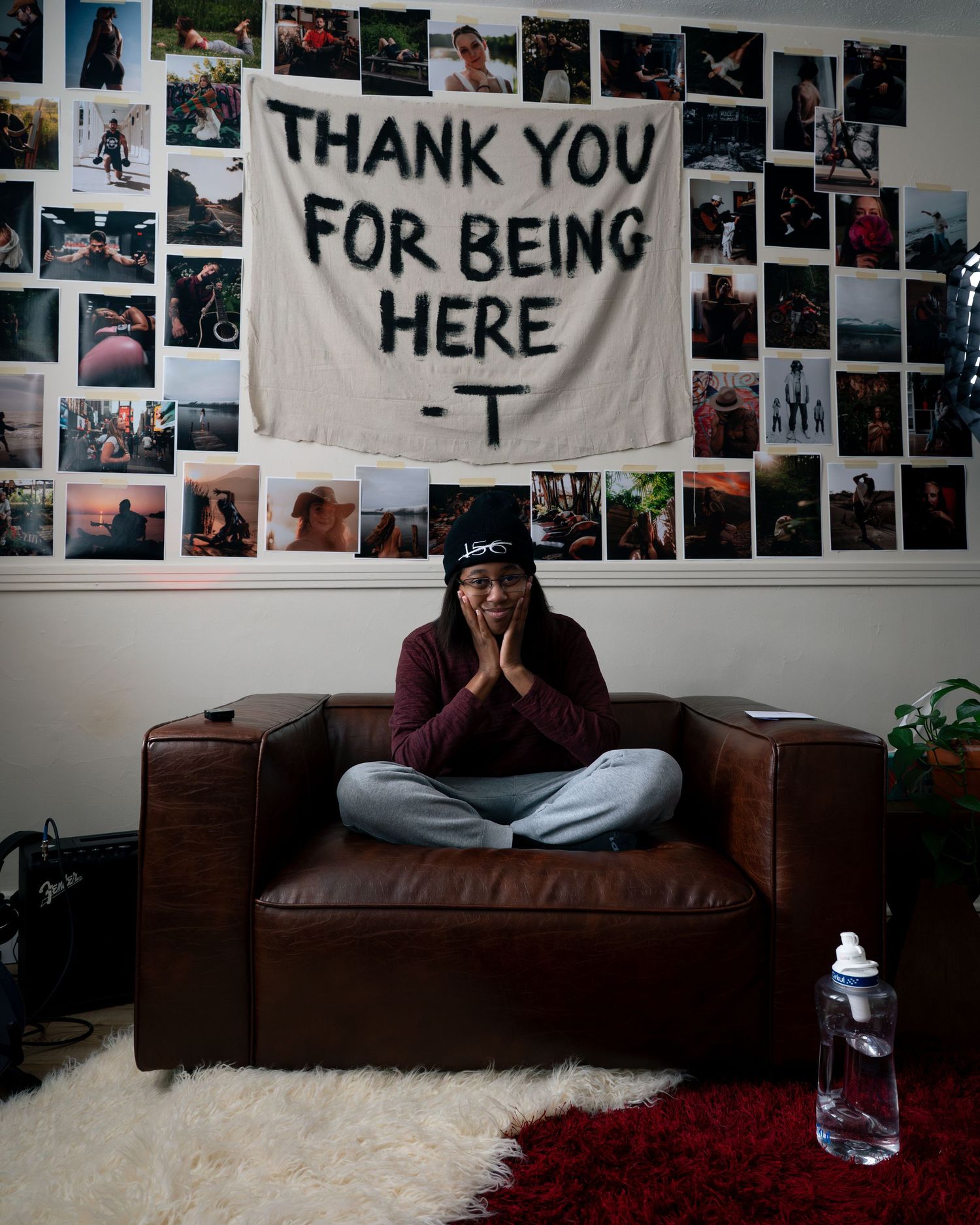 A cozy room interior with a brown couch and wall decorated with photos and a banner reading 'THANK YOU FOR BEING HERE'.