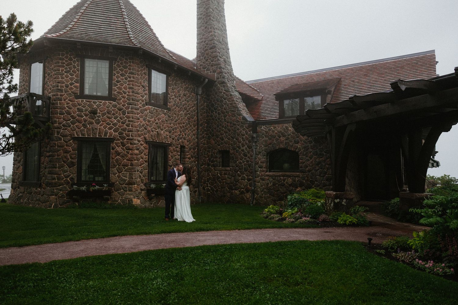 A couple walks along a stone path leading to a rustic brick building entrance at dusk.