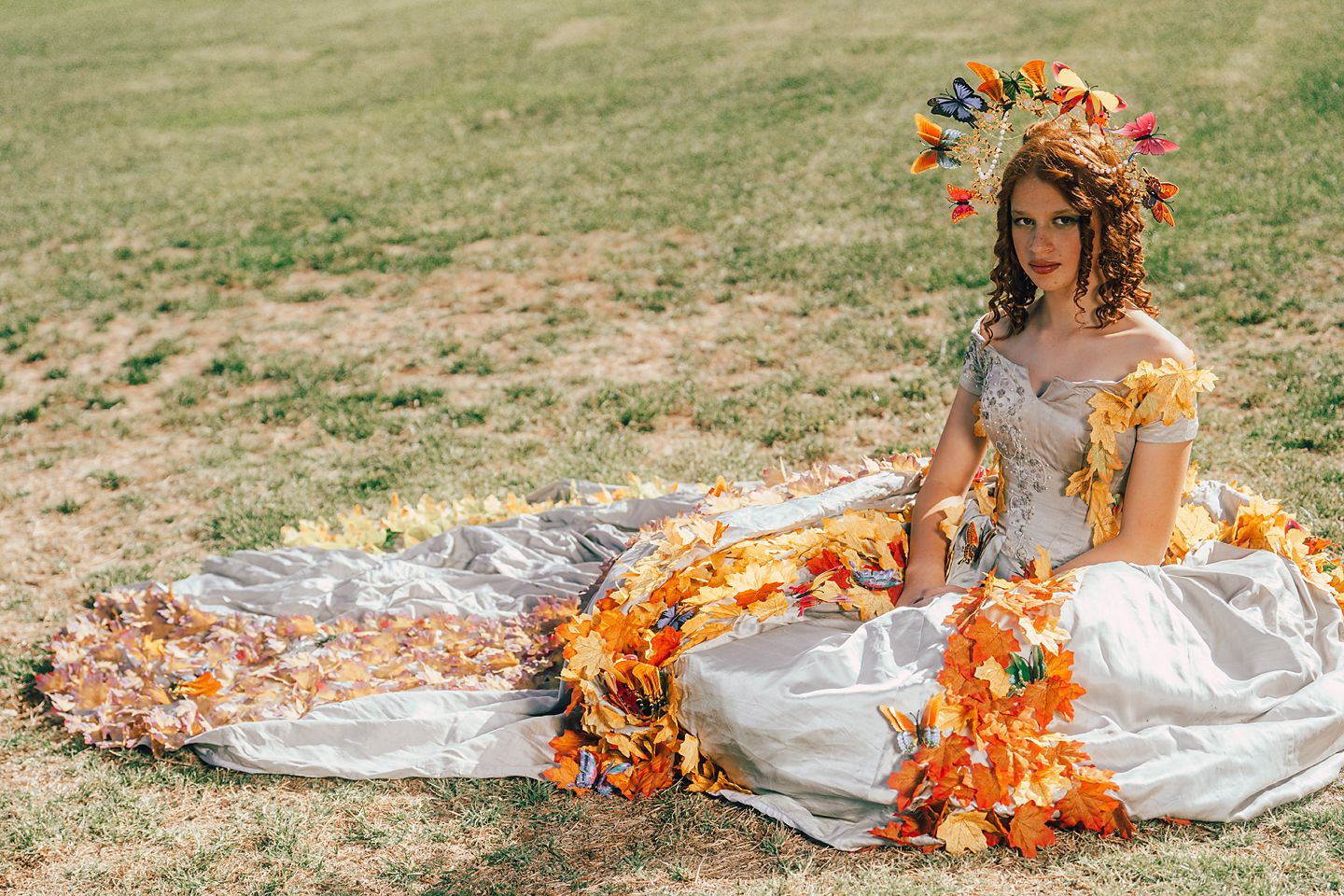 A silver dress with orange and red autumn flowers creates a dramatic fashion scene in a grassy field.