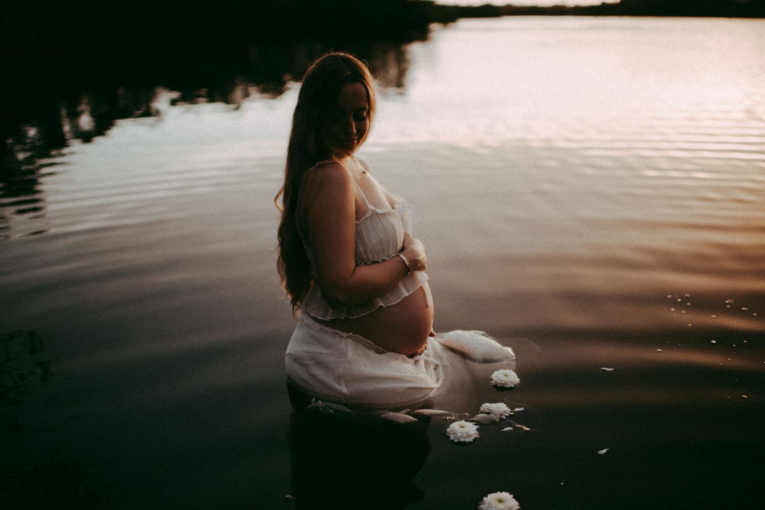 A silhouetted figure in a white dress sits by a tranquil lake at sunset creating a peaceful reflection on the water. sarasota beach photo