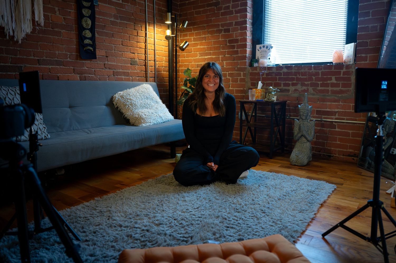 Relaxed person sits comfortably on green couch with yellow striped pillows in warm indoor lighting.