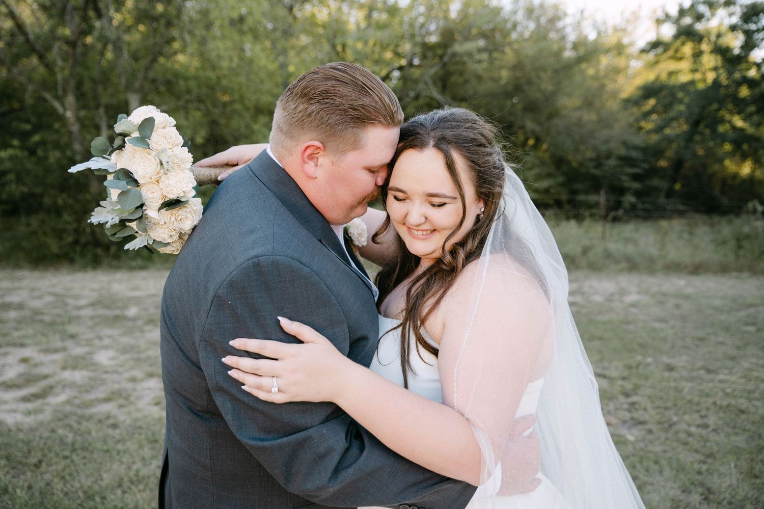 A happy couple at their wedding celebration with a beautiful floral bouquet featuring white and blue flowers in a rustic setting.