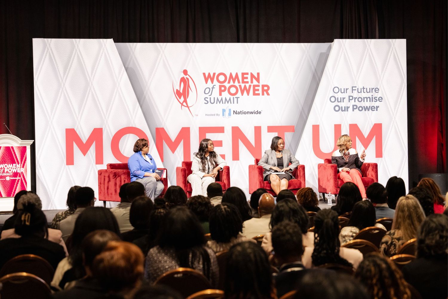 Panel discussion at Women of Power conference with speakers seated on stage addressing large audience.
