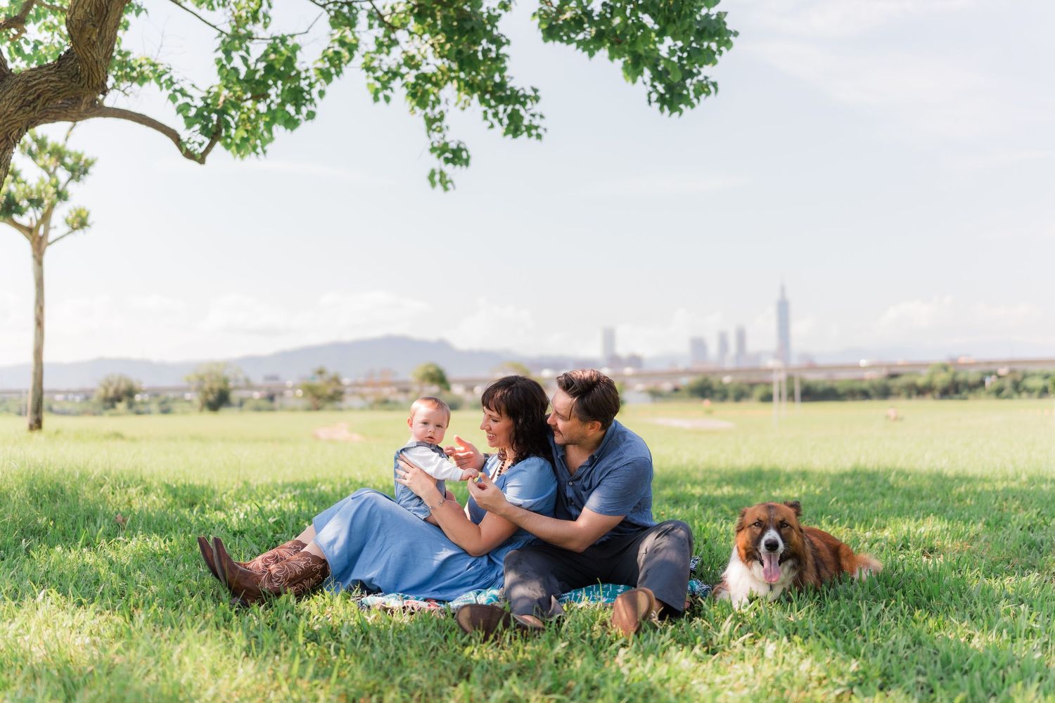 People relax on grassy hillside with dog while enjoying sunny day in countryside.