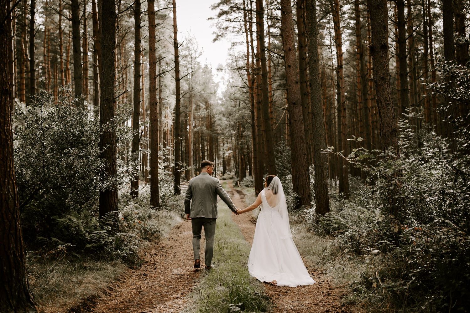 A couple walks through a misty forest setting during their wedding photo session in elegant formal attire.